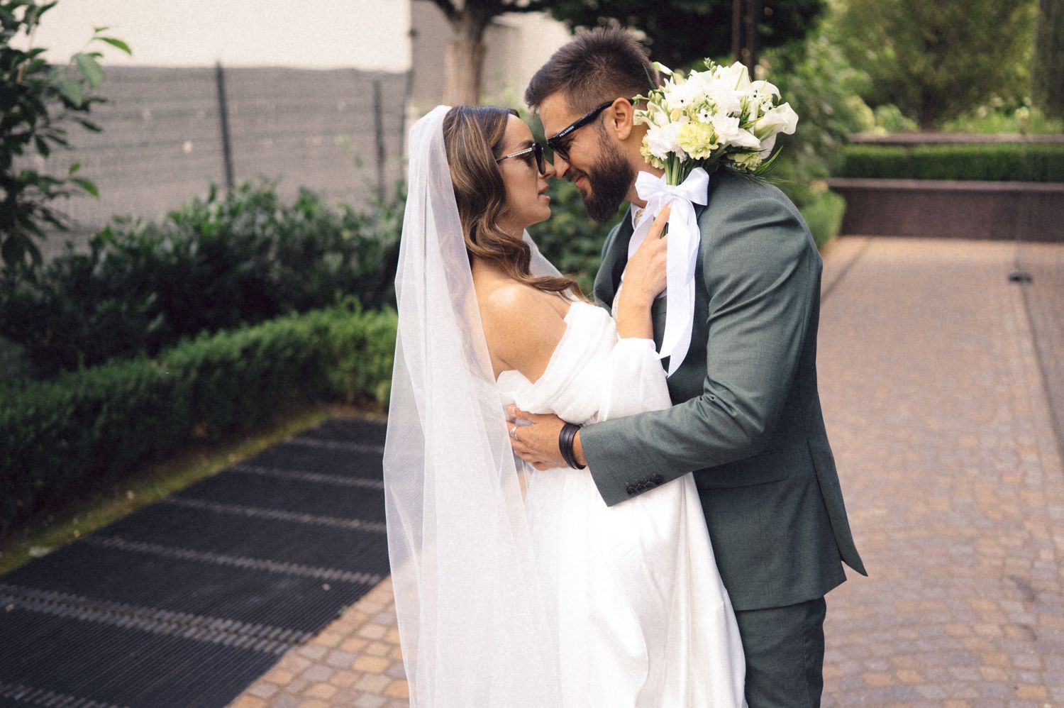 A romantic wedding couple shares an intimate moment together on a brick pathway surrounded by greenery.