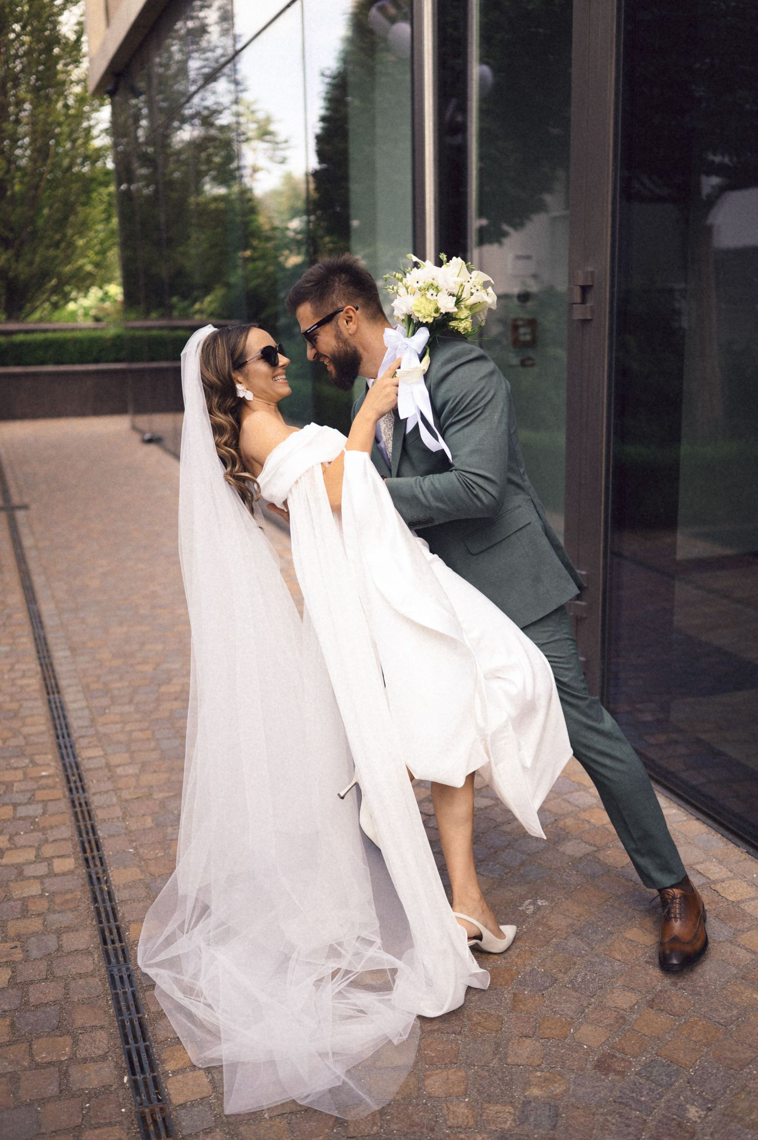 A romantic wedding couple shares a tender moment while dipping in a choreographed dance pose outside a building.