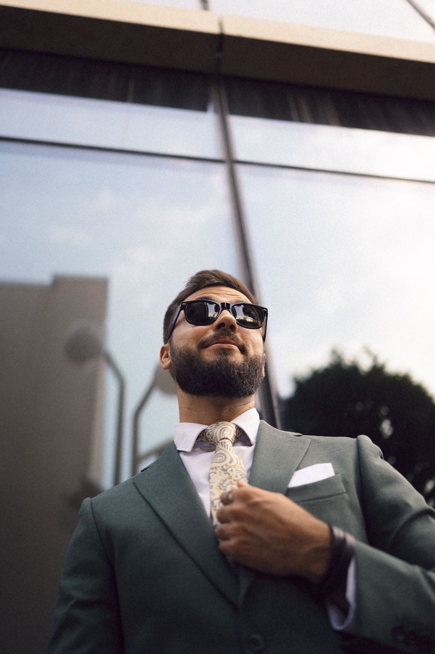 A person wearing sunglasses and a green suit adjusts their tie in a series of connected photos.