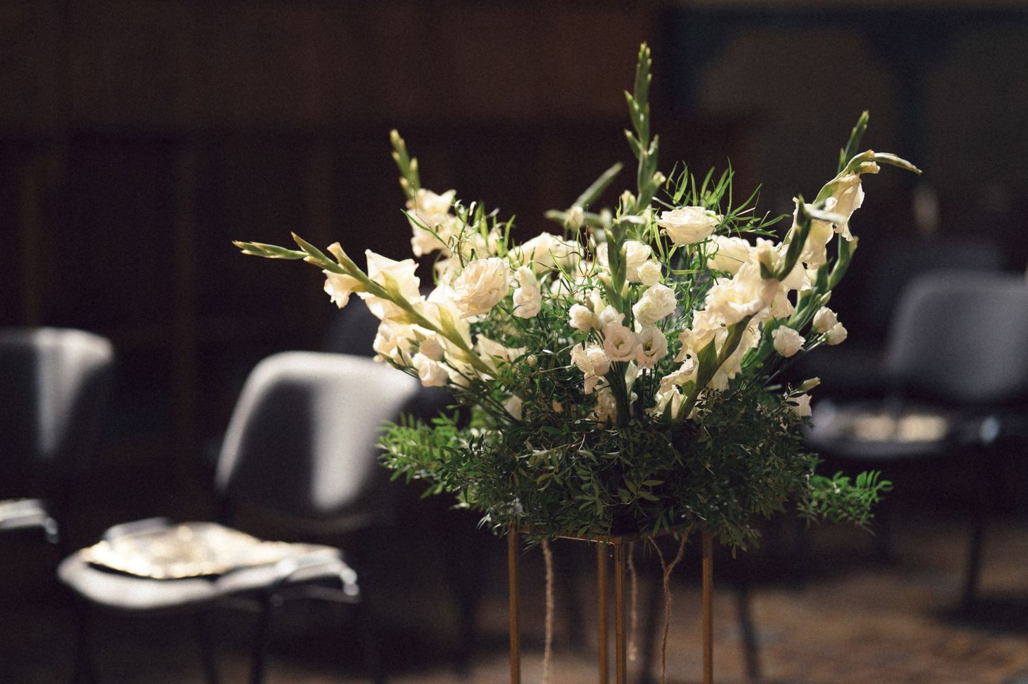 A row of elegant floral centerpieces with white blooms and greenery arranged in clear glass vases for a formal event.