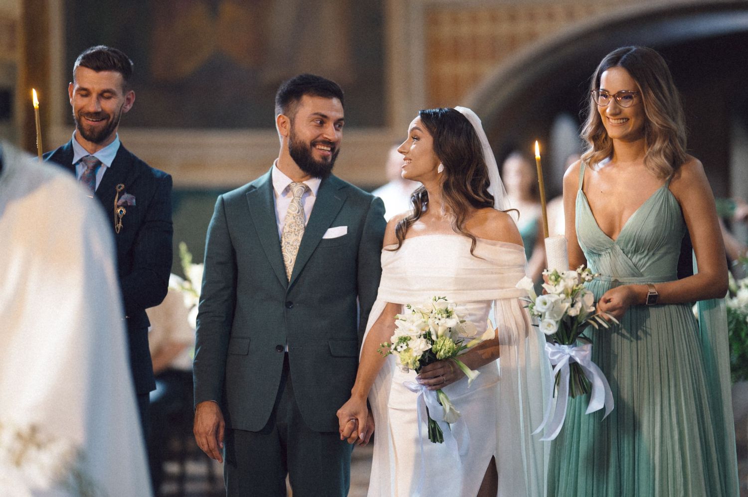 Wedding party in sage green and gray attire walks together while holding bouquets during outdoor ceremony.