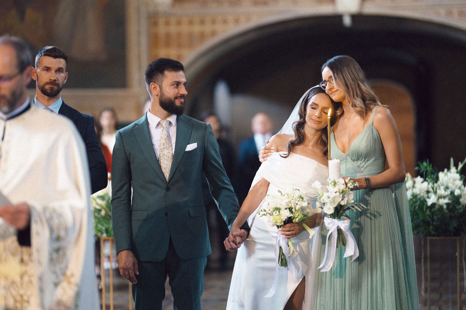 Wedding party in sage green dresses and navy suits gather for formal photos at an elegant venue.