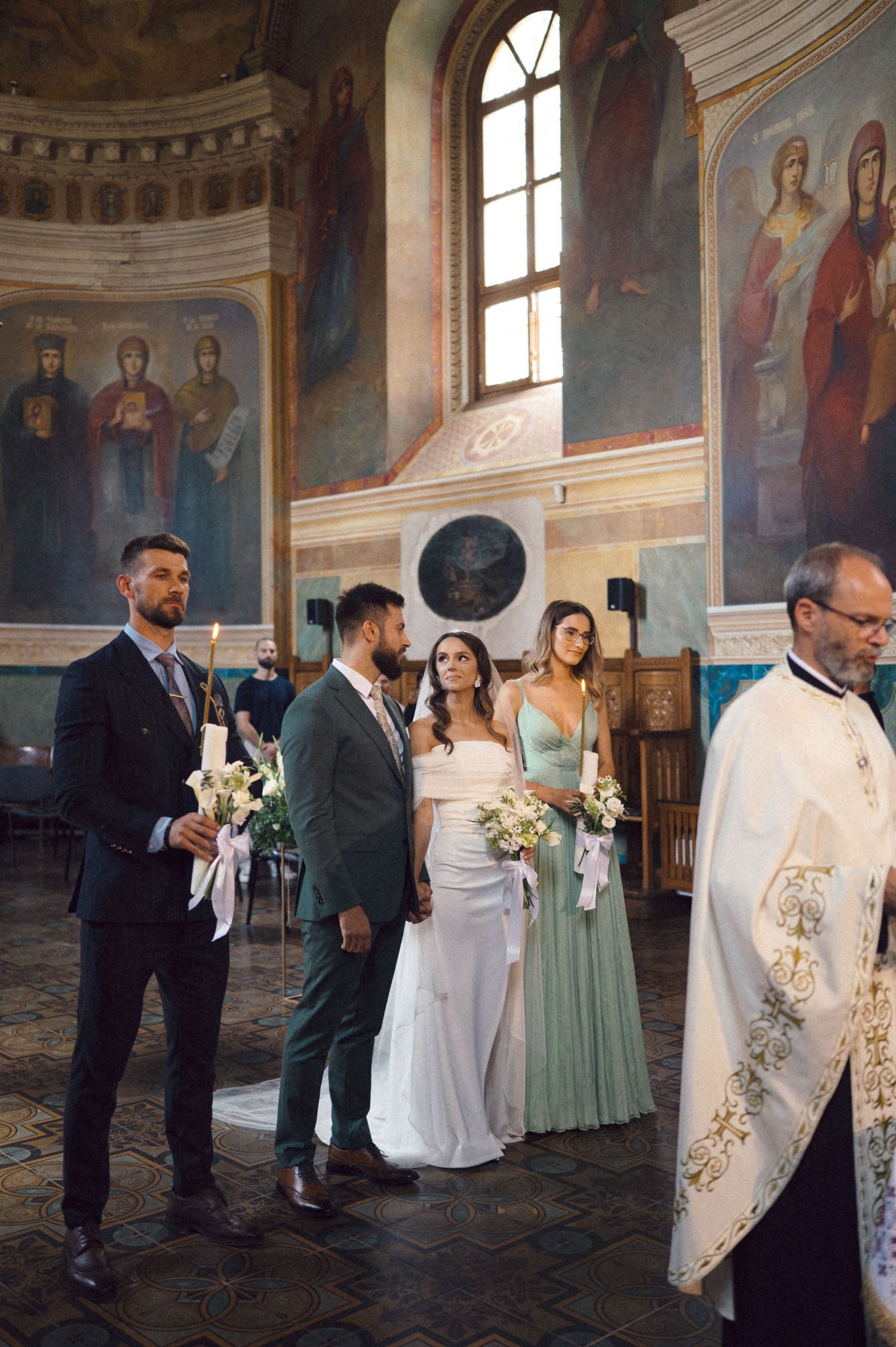 Wedding party lines up inside an ornate church with religious murals and arched windows during a ceremony.