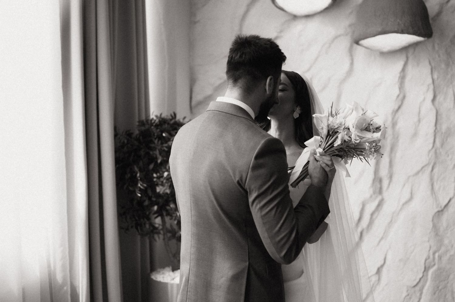 Black and white romantic wedding photos showing intimate moments between newlyweds against a white wall.