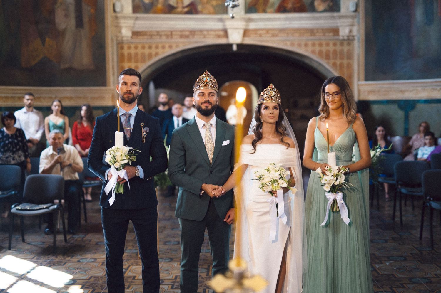 Wedding party poses together in formal attire with bridesmaids wearing sage green dresses and holding bouquets.