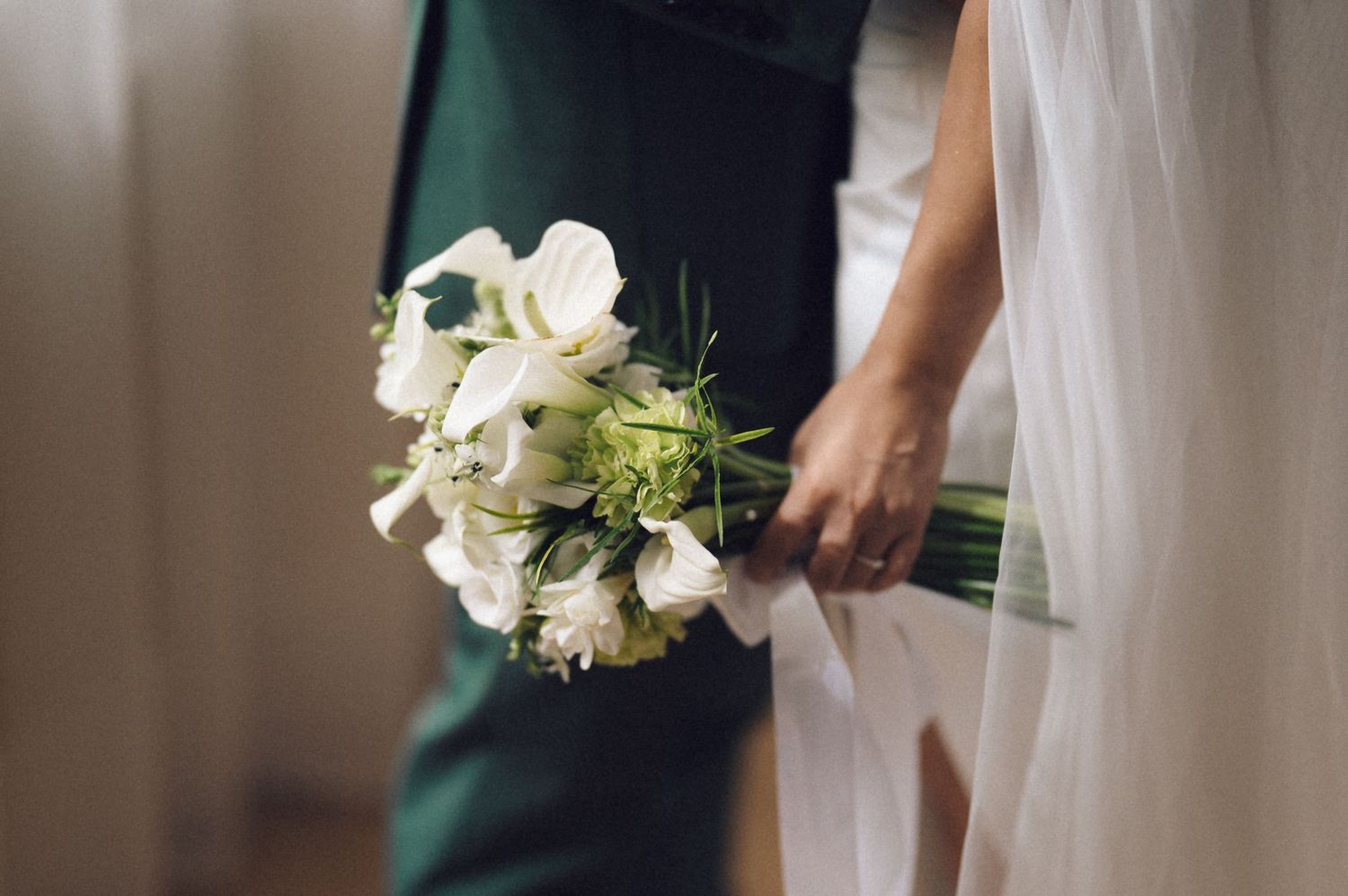Bridesmaids in dark green dresses holding white floral bouquets stand in a line.