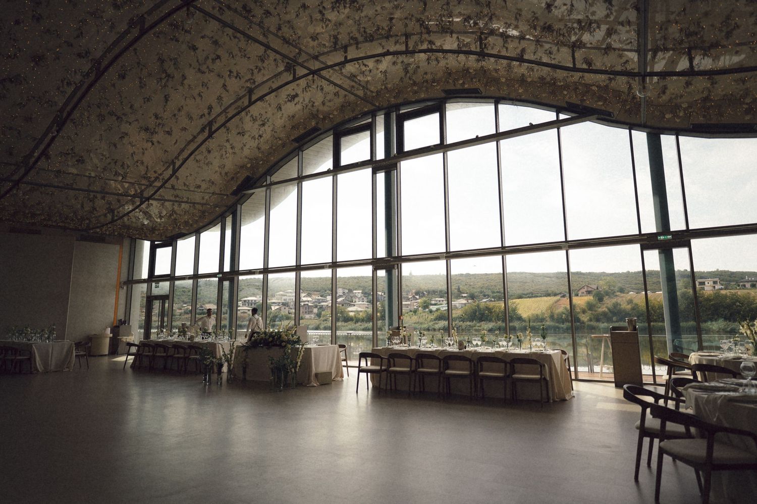 A panoramic view of a modern building interior with curved glass walls and concrete ceiling overlooking a city landscape.