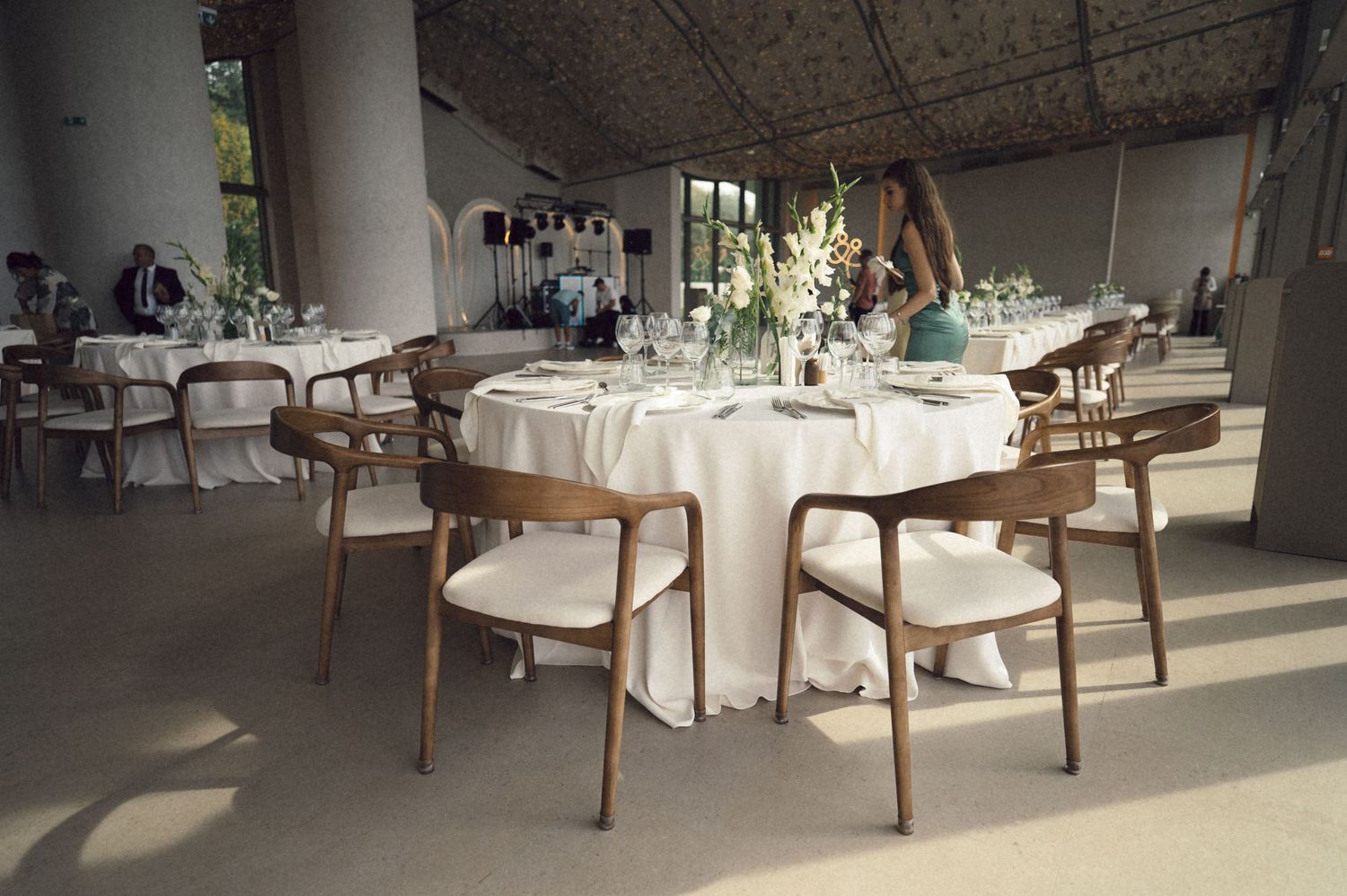 Elegant wedding reception venue with white tablecloths and wooden chairs in a sunlit room with polished floors.