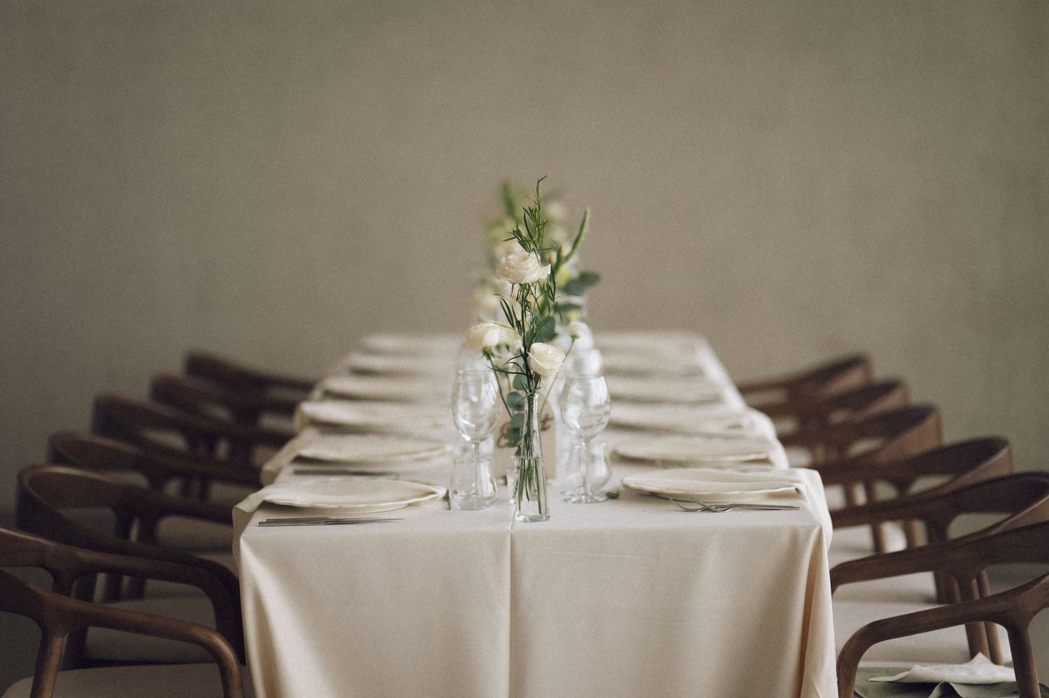 Elegant table settings with white linens, dark wooden chairs, and delicate floral centerpieces in a restaurant dining room.