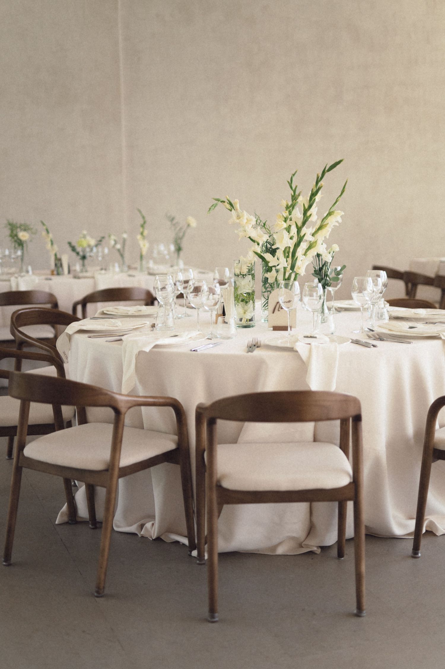 Elegant dining room setup with round tables covered in white tablecloths and modern wooden chairs in a minimalist space.