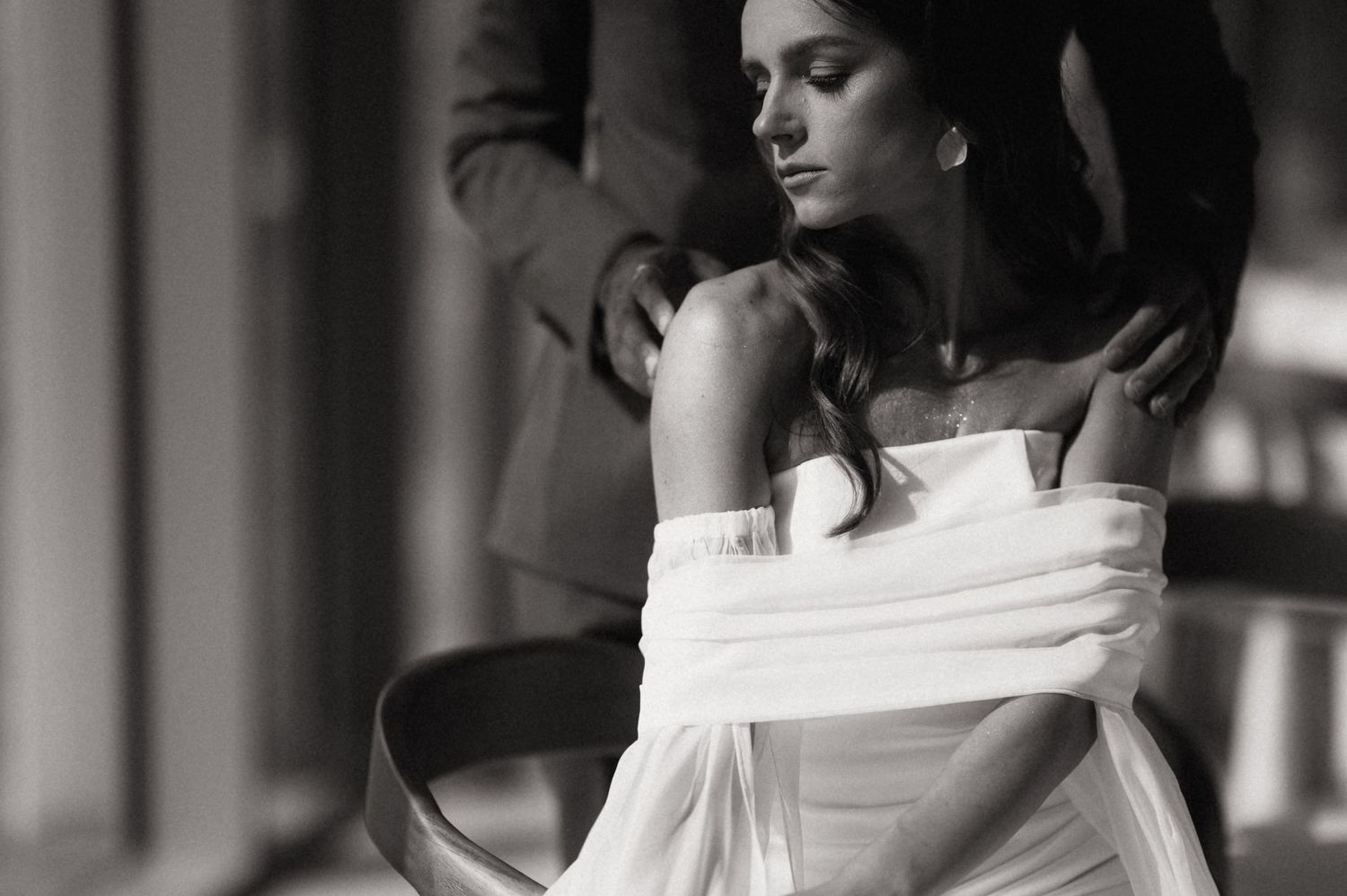 Black and white photo of a person in a white dress sitting in a chair, looking down pensively.