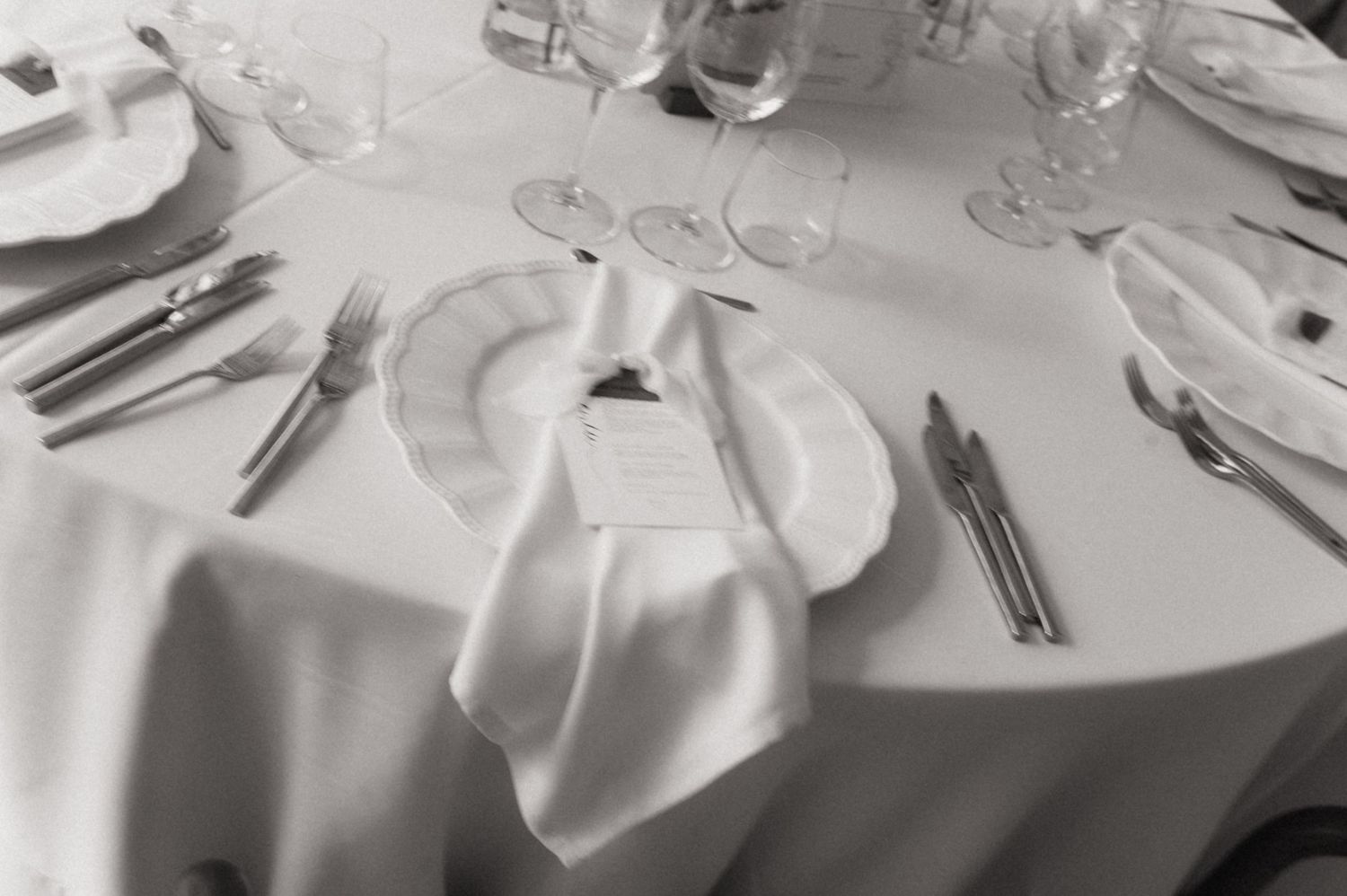 Elegant formal dining table setting with white linens, silverware, and wine glasses on round table.
