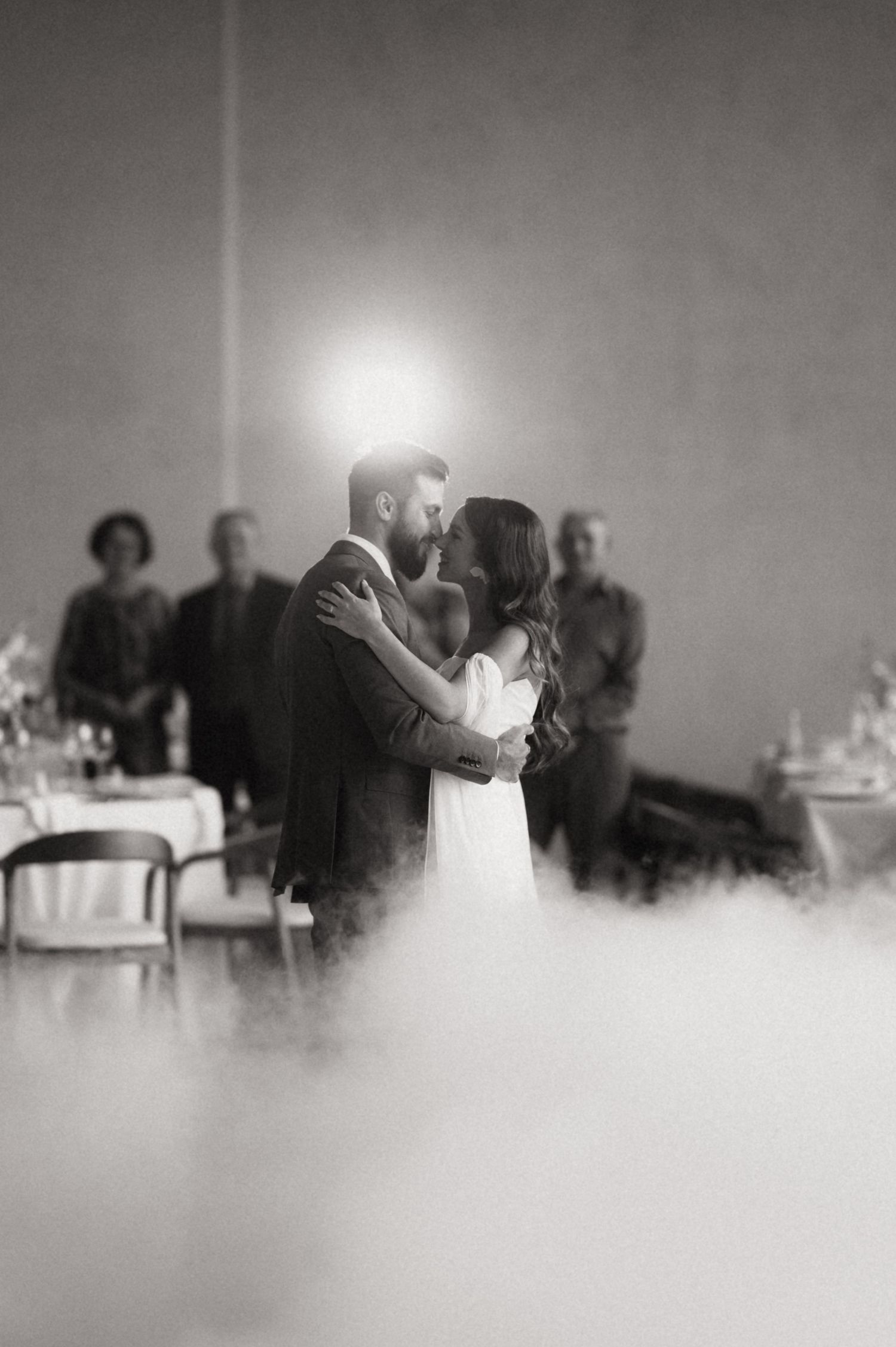 A romantic black and white wedding photo of a couple sharing their first dance with guests watching in the background.