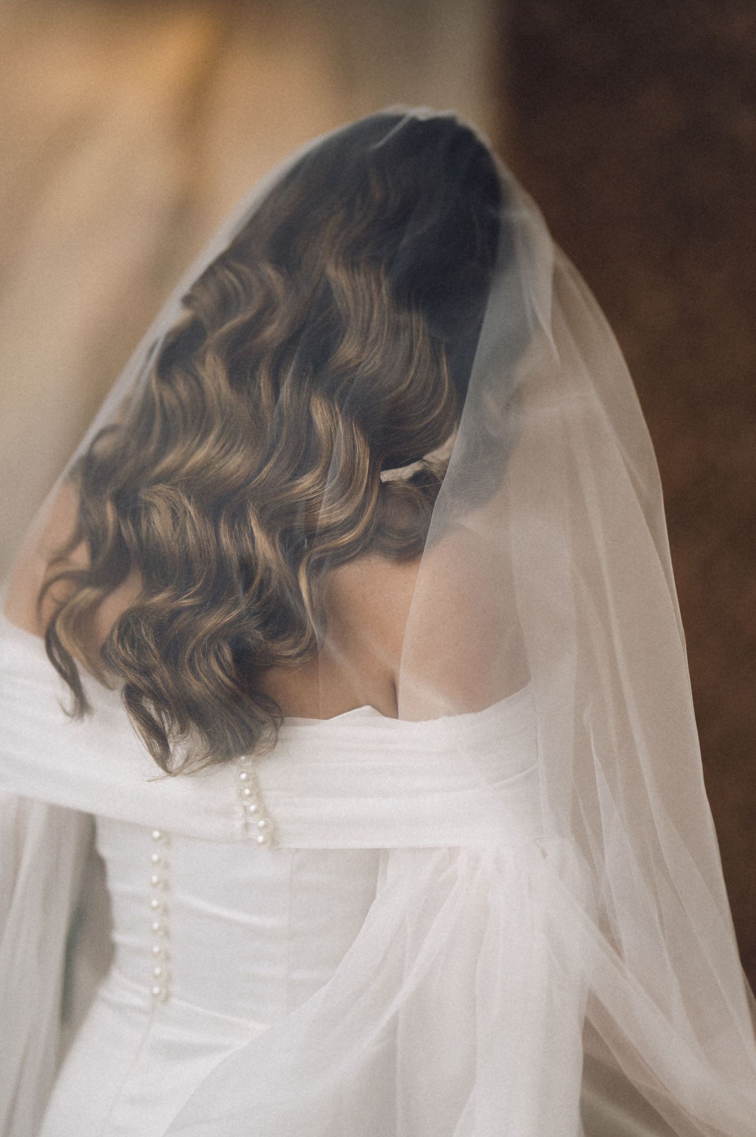 Close-up view of a bride's white wedding dress with button details and flowing veil.