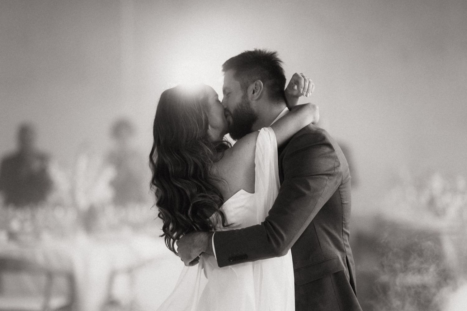 A romantic black and white wedding photo shows a couple sharing a kiss with sunlight glowing behind them.