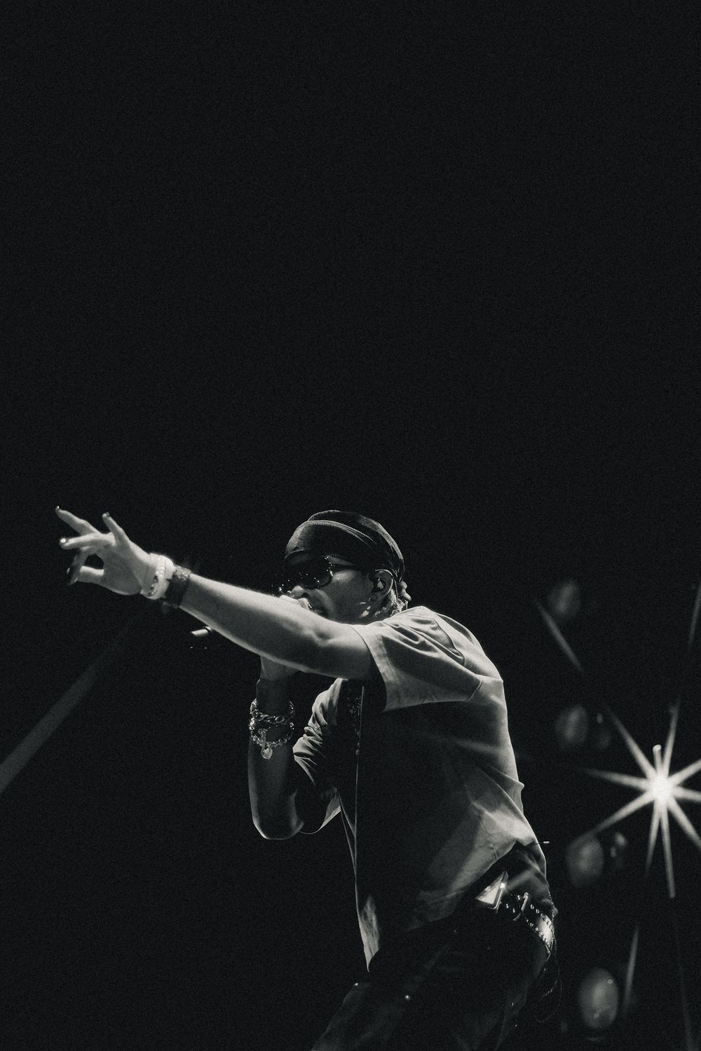 Silhouetted performer gestures dramatically against dark concert backdrop with bright spotlights.