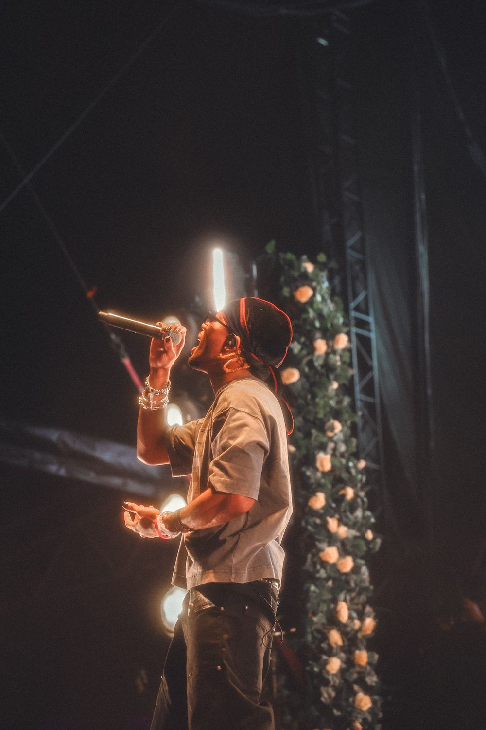 Concert performer in casual attire illuminated by warm stage lighting amidst floral decorations.