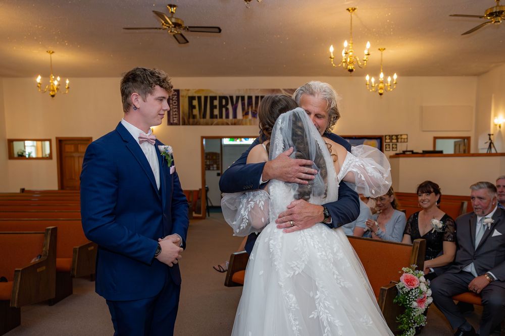 A joyful wedding reception moment captured in dim lighting with guests dancing and celebrating in an elegant banquet hall.