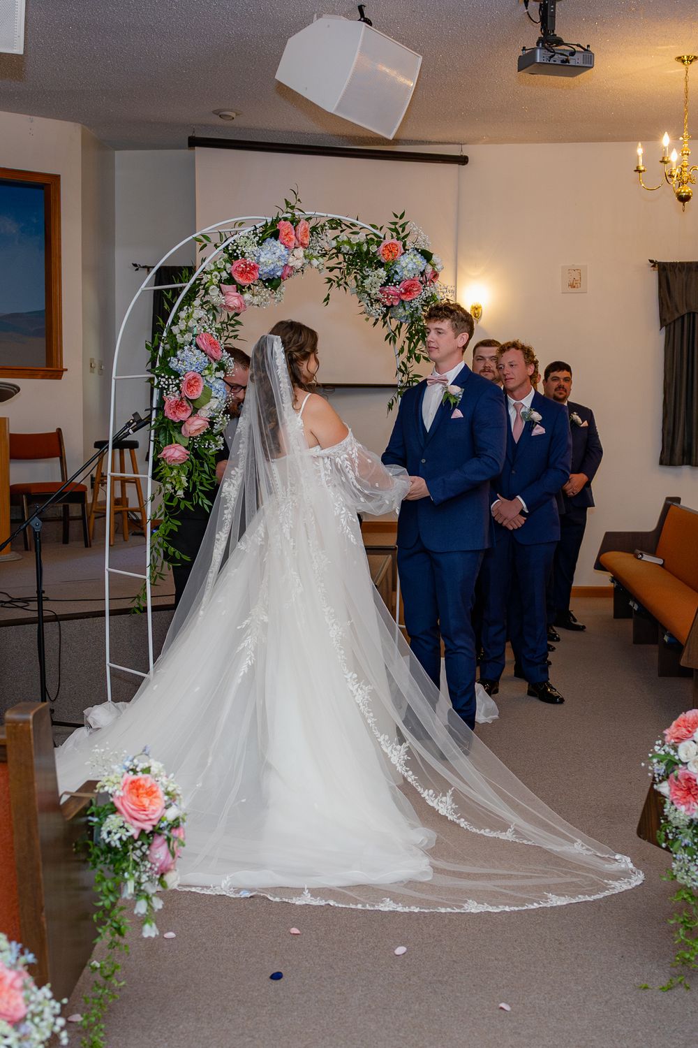 Wedding ceremony in a chapel with a floral arch decorated in pink and white roses and delicate greenery.