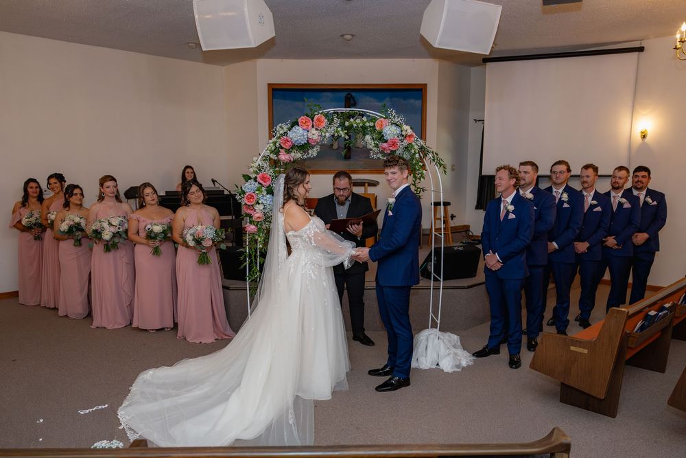 Wedding party in formal attire stands in a row in a spacious banquet hall during a wedding ceremony.