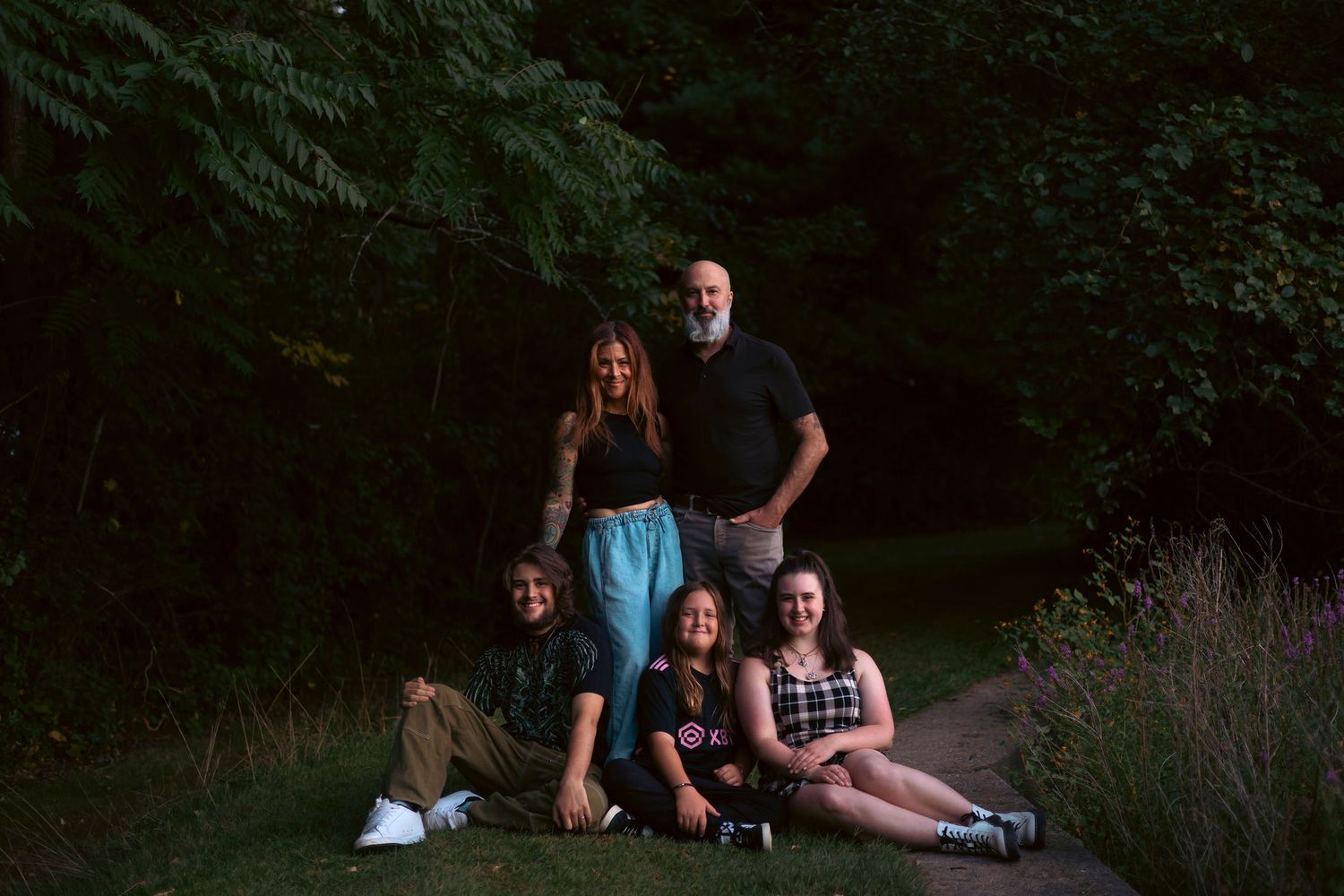 Family members sitting together in a wooded outdoor setting during a casual photo session.
