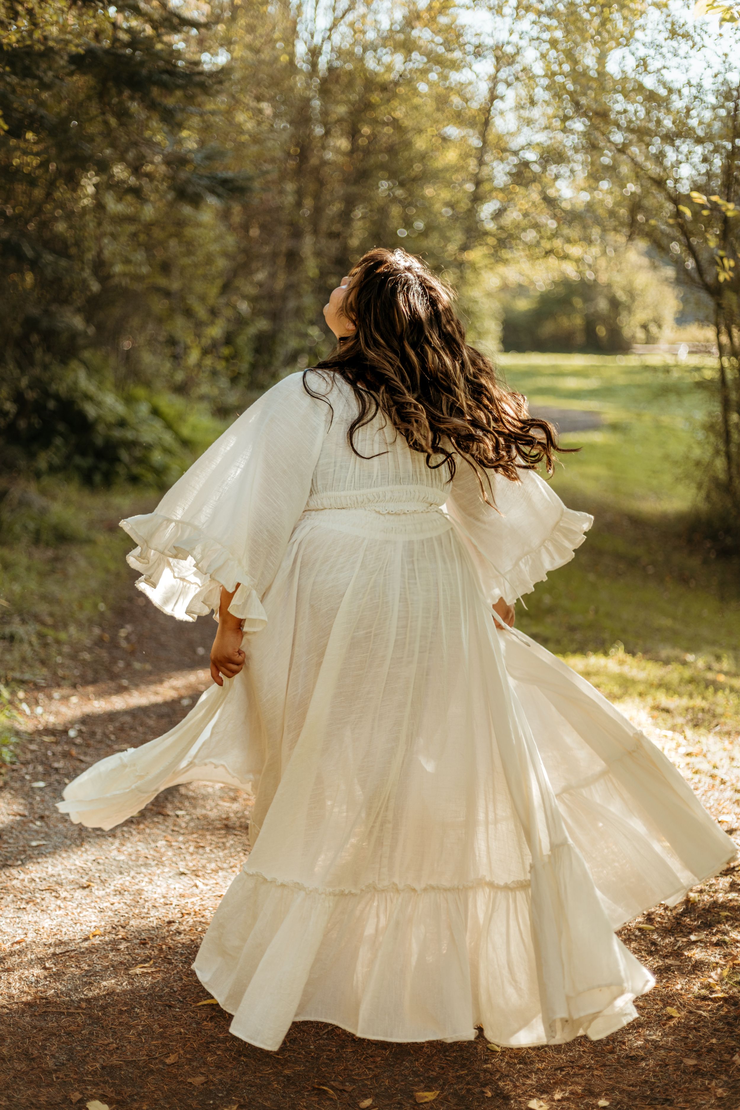 A flowing white vintage-style dress twirls in a sunlit autumn forest setting, creating an ethereal motion effect.