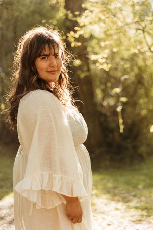A person in a white ruffled dress poses outdoors in soft golden sunlight during a photo session.