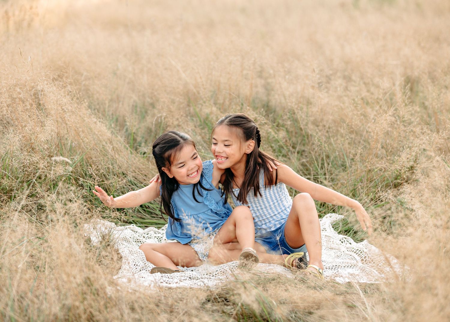 Family lying together on a blanket in a golden field during sunset.