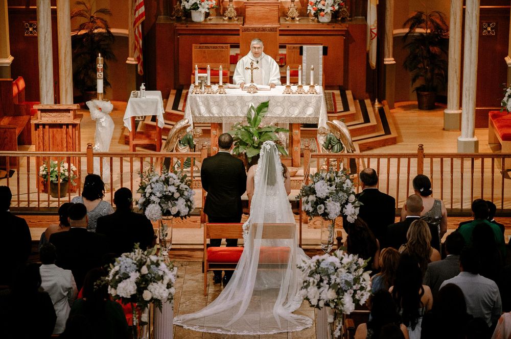 Traditional church wedding ceremony with white floral arrangements and long flowing veil in a wooden chapel setting.