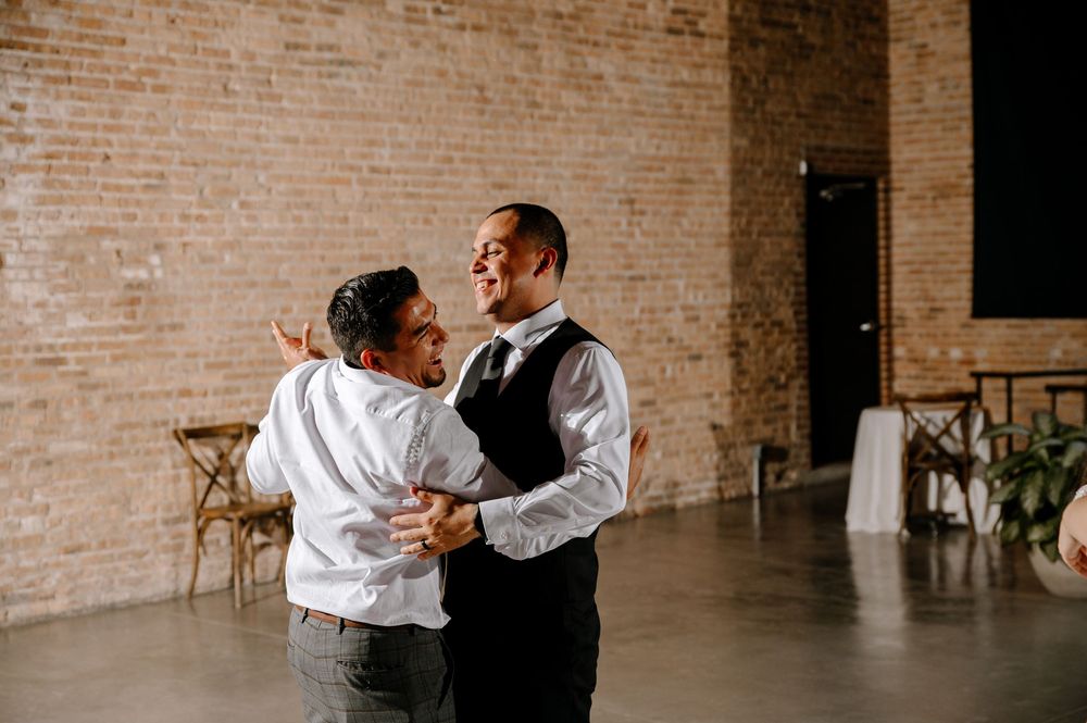 Two dancers perform a dramatic contemporary dance movement in a rustic brick-walled studio space.
