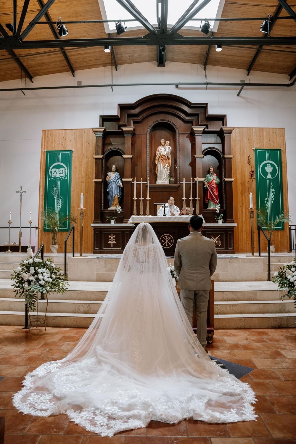 A wedding ceremony in a church with a long flowing white bridal gown train displayed across the tile floor.