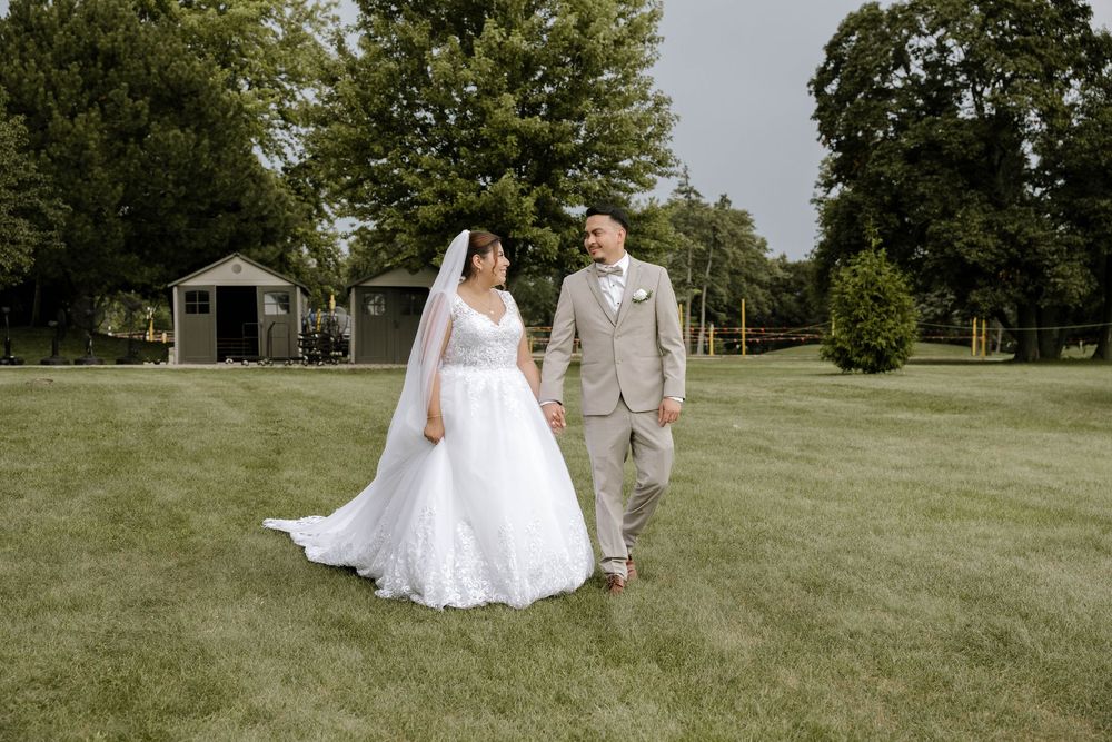 A couple in wedding attire walks together across a lush green lawn on their special day.