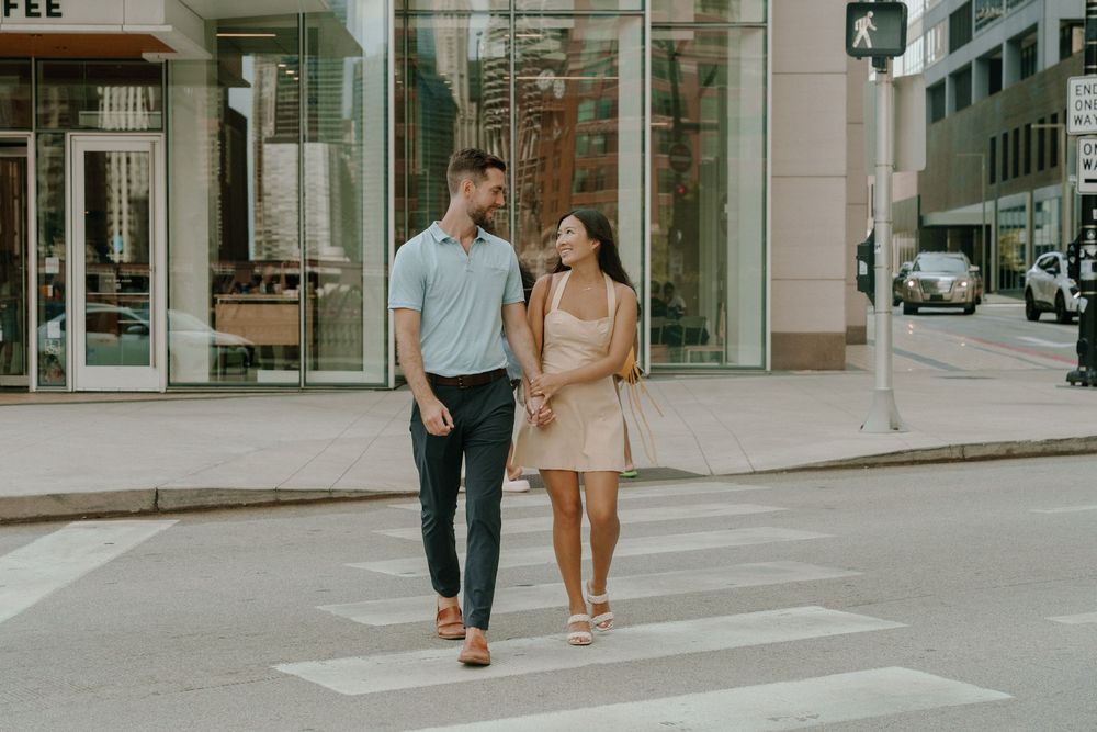 Couple walking hand in hand on an urban sidewalk with storefronts visible in the background.