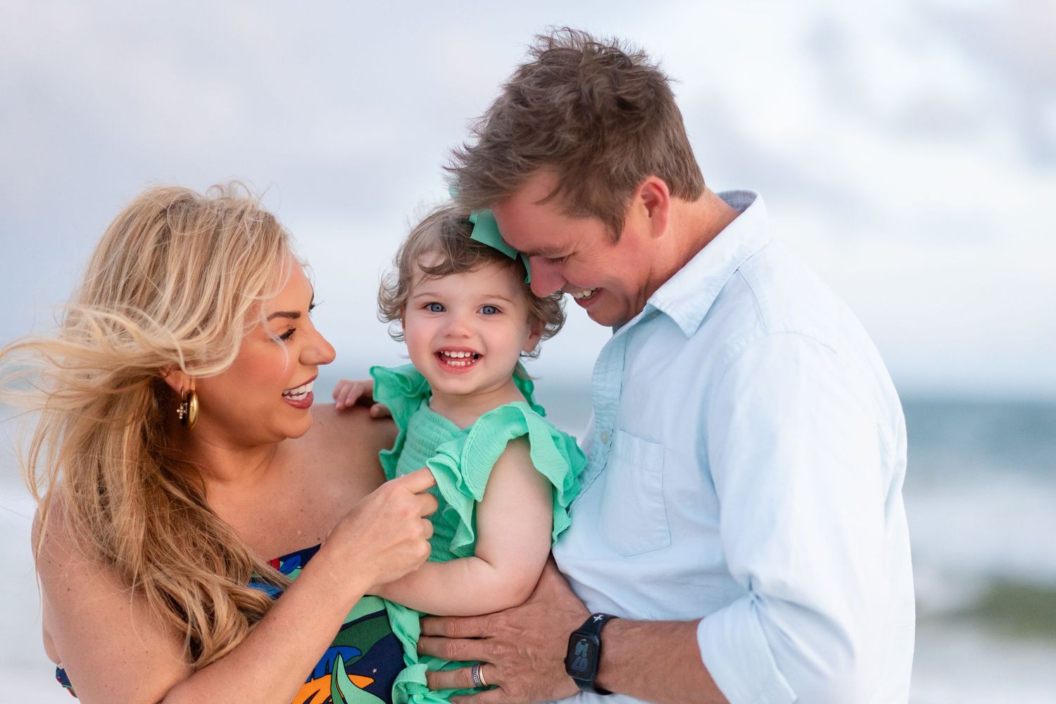 Family enjoying a tender moment together on a sunny beach with waves in the background.