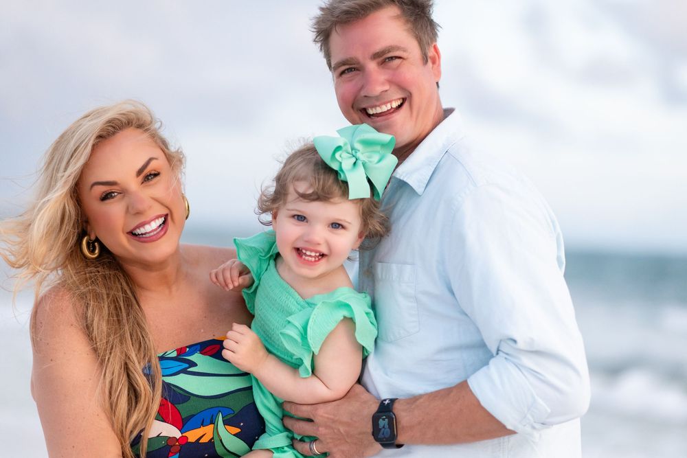 Three people share joyful laughter during a casual beach portrait session at the ocean.