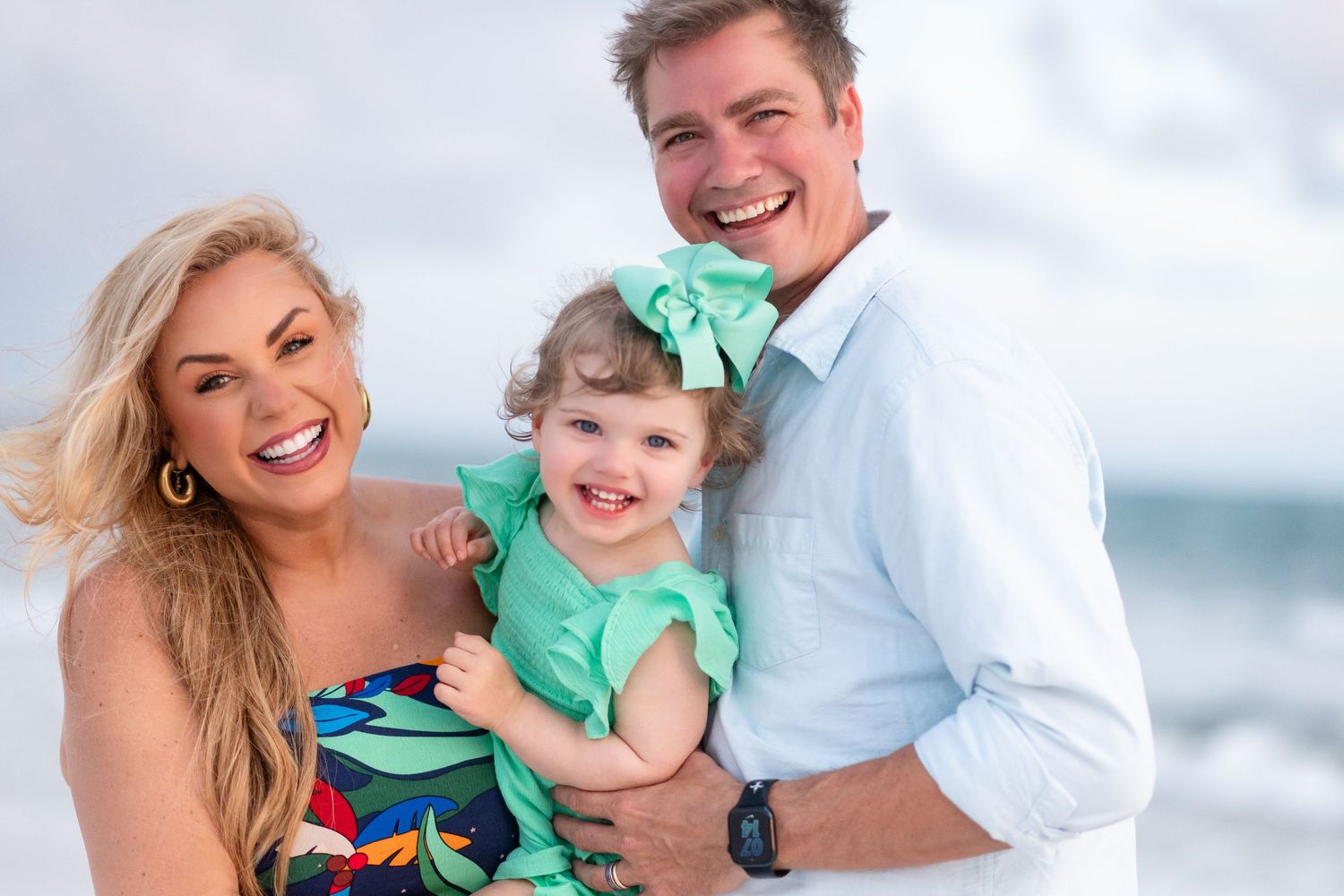 Three people share joyful laughter during a casual beach portrait session at the ocean.