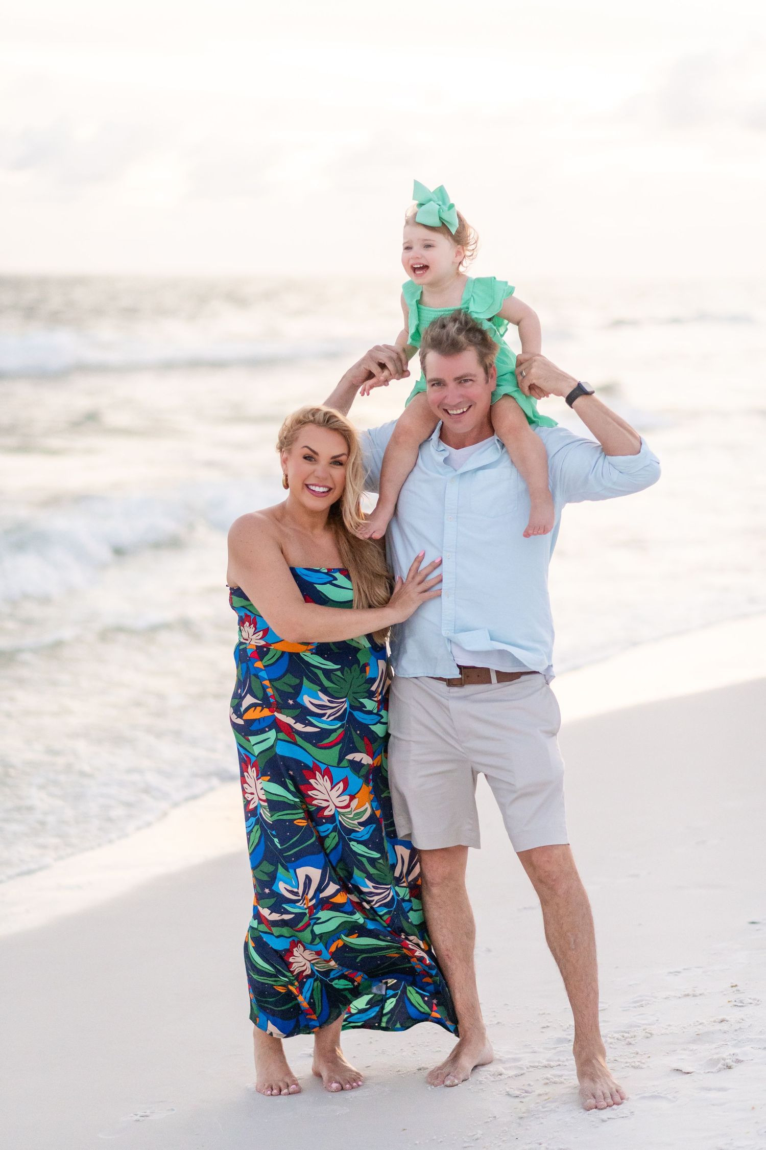 Couple enjoying a playful moment together on a sunny beach wearing tropical print dress and casual beachwear.
