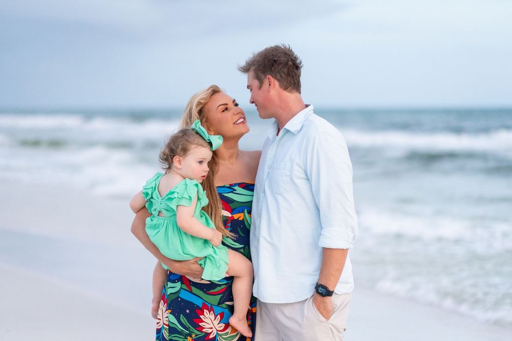A family embraces while posing for a portrait on the beach with ocean waves in the background.
