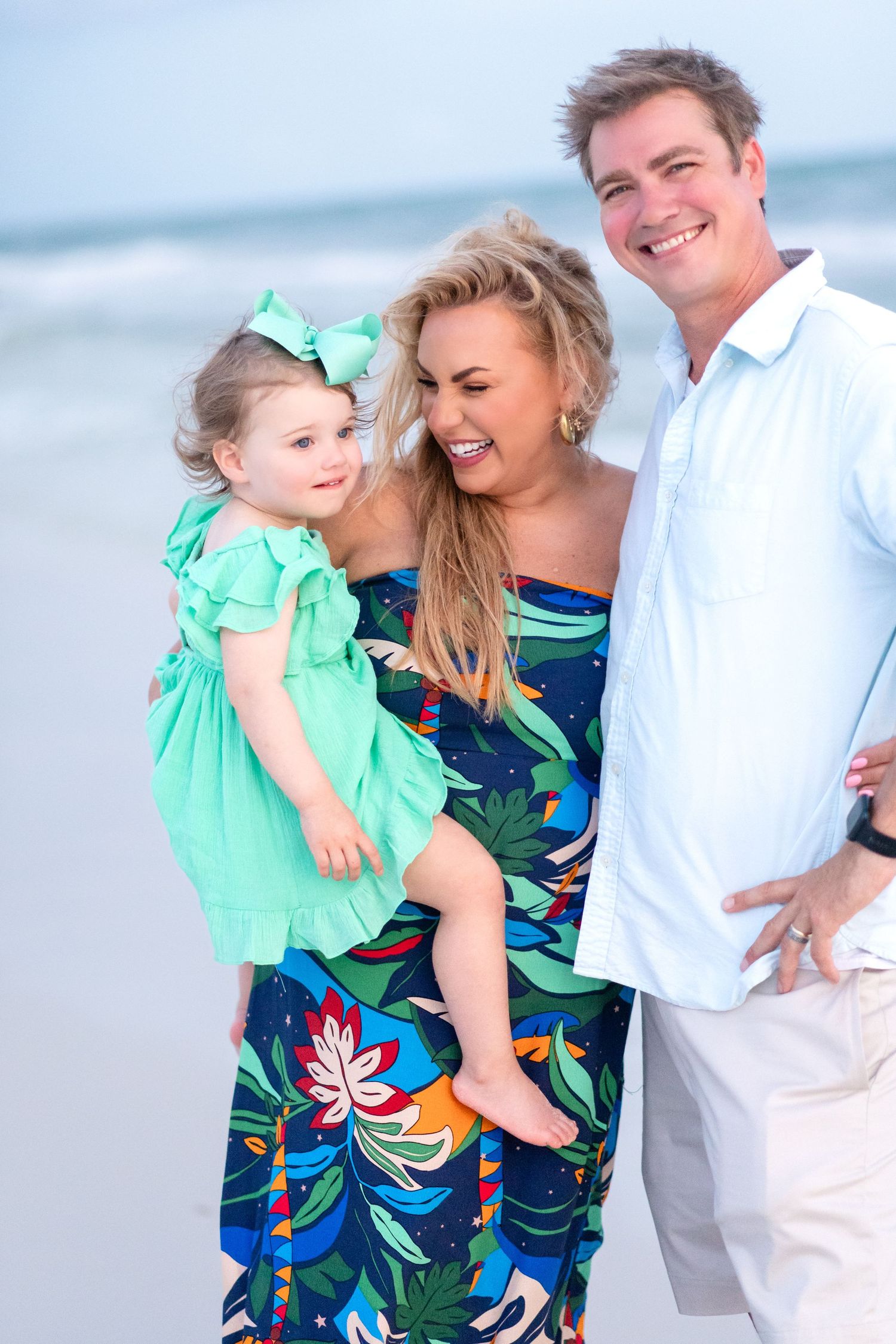 A family enjoys a sunny day at the beach wearing coordinated outfits in mint green and navy blue tropical print.