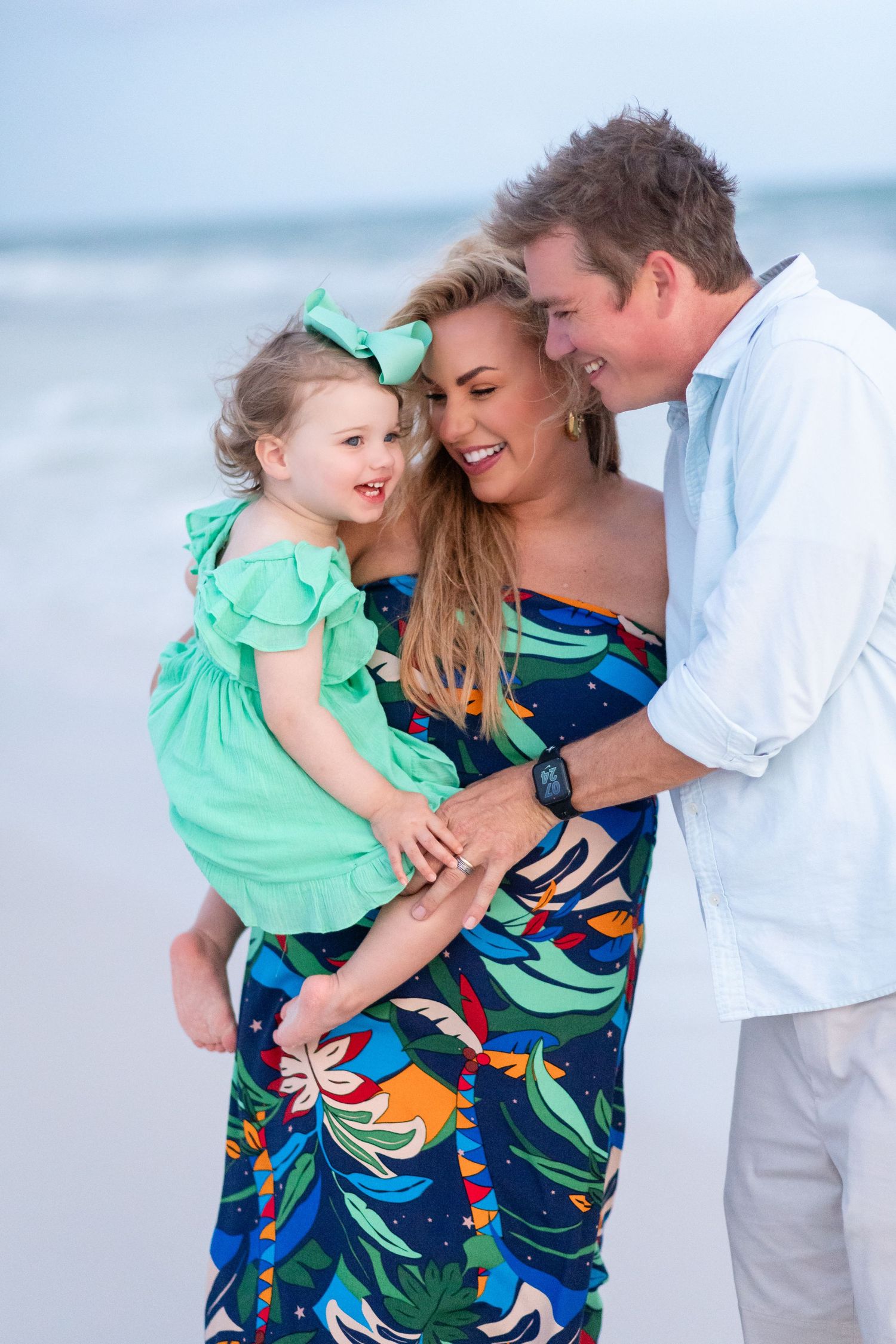 Family wearing coordinated blue and mint green outfits share joyful moments together on a sunny beach.