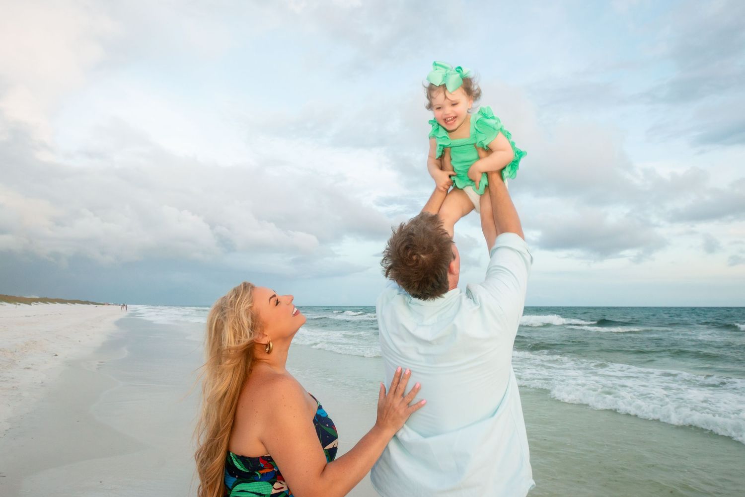 Couple sharing a romantic moment on the beach with waves and cloudy sky in the background.