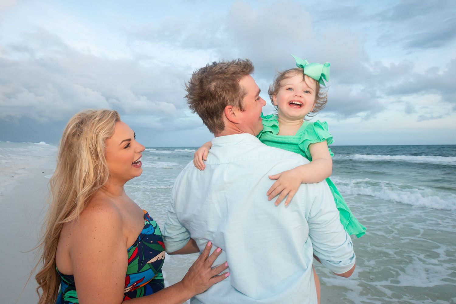 A family enjoys a tender moment together on a cloudy beach with waves crashing in the background.