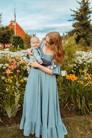 A parent and child wearing matching blue dresses pose together in a garden with blooming flowers and lilies.