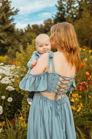 A pair wearing matching light blue dresses with ruffle details stand in a garden with daisies and lilies.