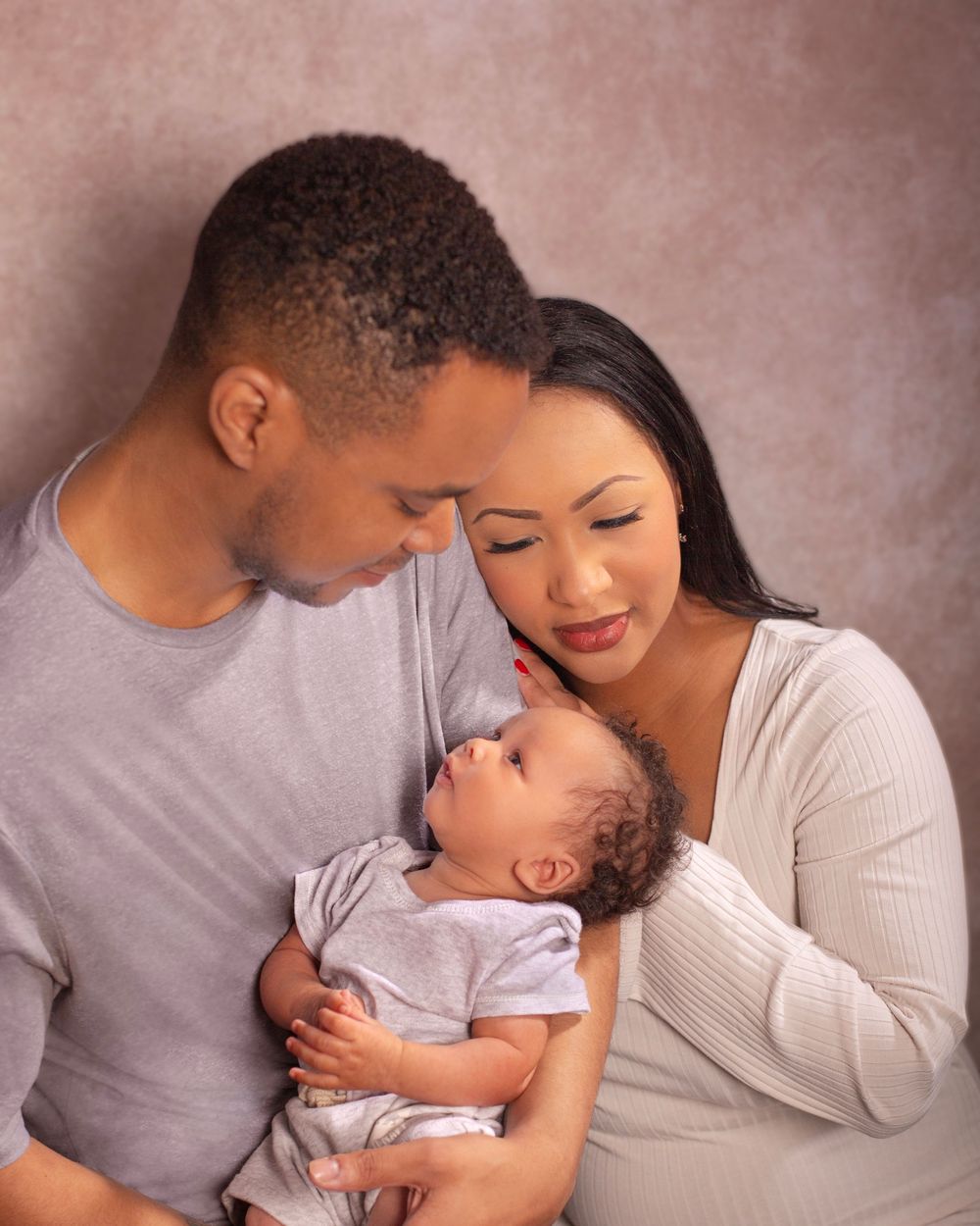 A tender parenting moment captured showing affection, comfort and bonding in a soft-lit studio setting.