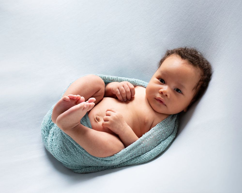 Peaceful sleeping newborn baby swaddled in soft turquoise blanket against light background.