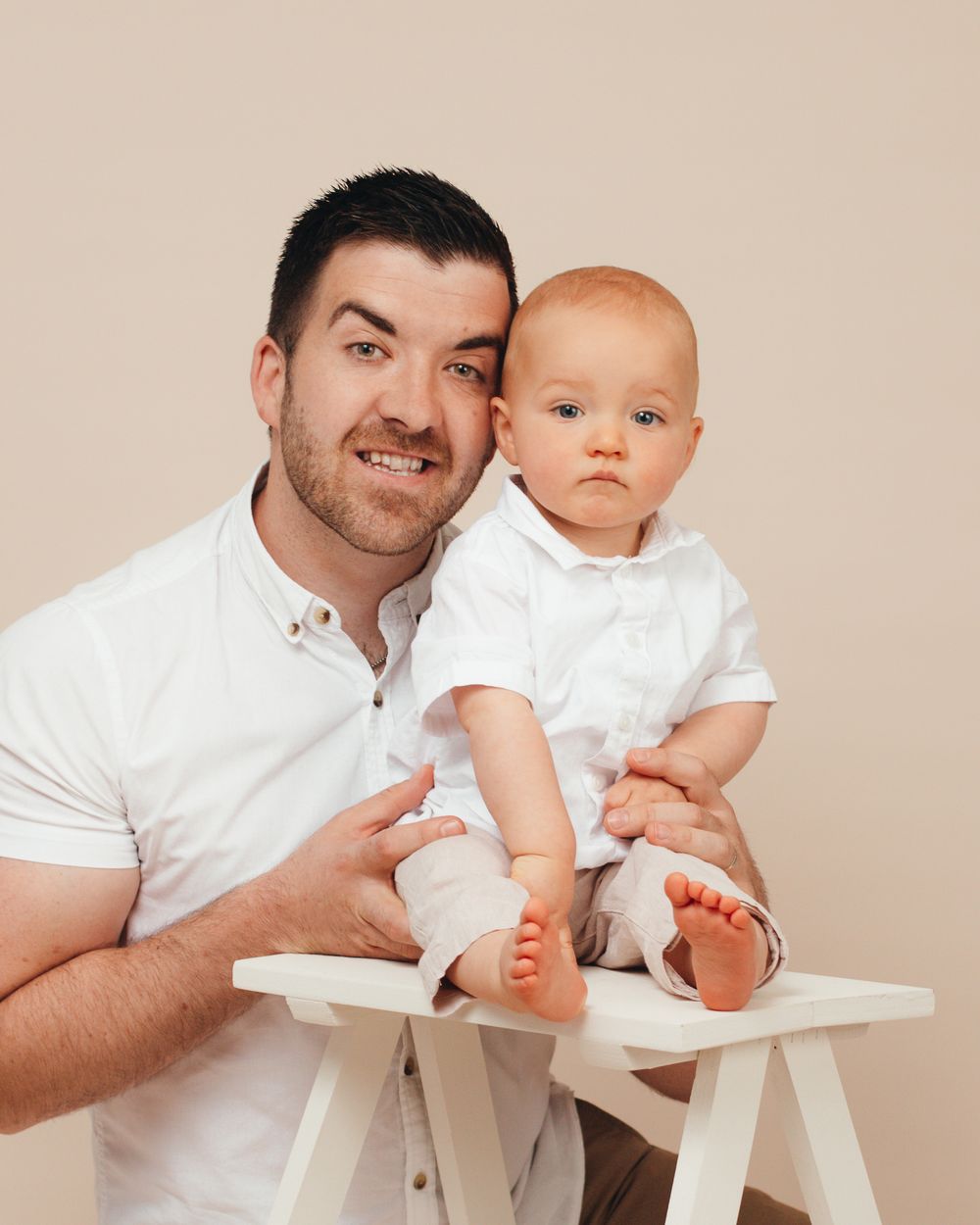 Parent and baby dressed in white share heartwarming moments while sitting at a small white table.