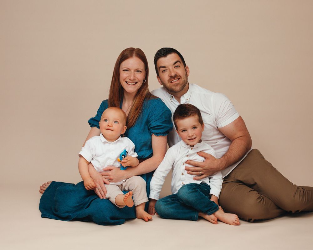 Family sitting and relaxing together in natural tones on beige backdrop during indoor photo session.