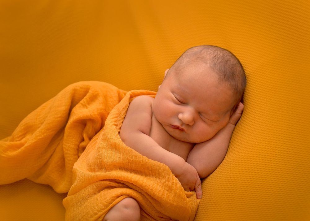 Newborn baby wrapped in orange blanket with bright orange background creating a warm, peaceful mood.