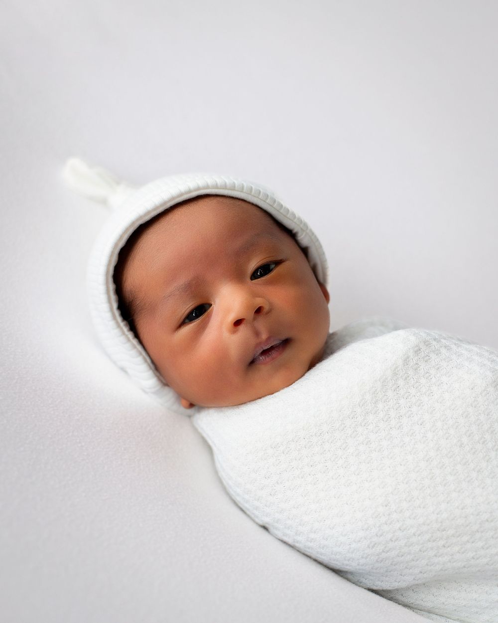A newborn baby swaddled in a white blanket is shown in a series of close-up shots while resting peacefully.